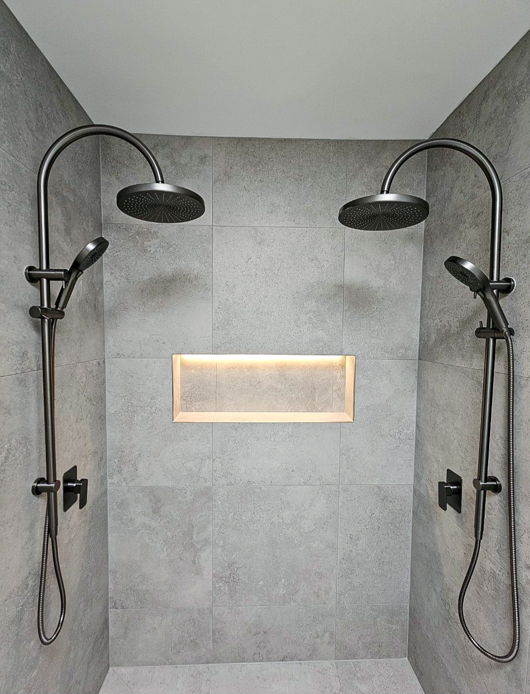 Bathroom renovation in Melbourne with twin rain shower heads, grey stone-look tile and a backlit niche