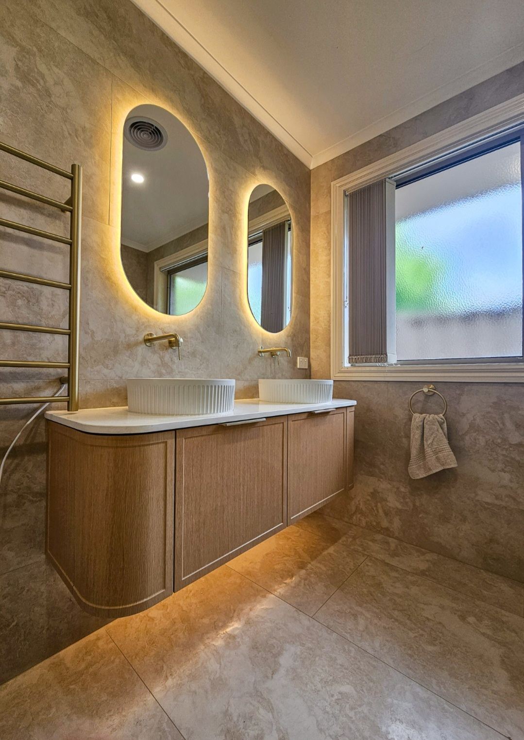 Double vanity bathroom renovation in Melbourne with backlit oval mirrors and brass tapware