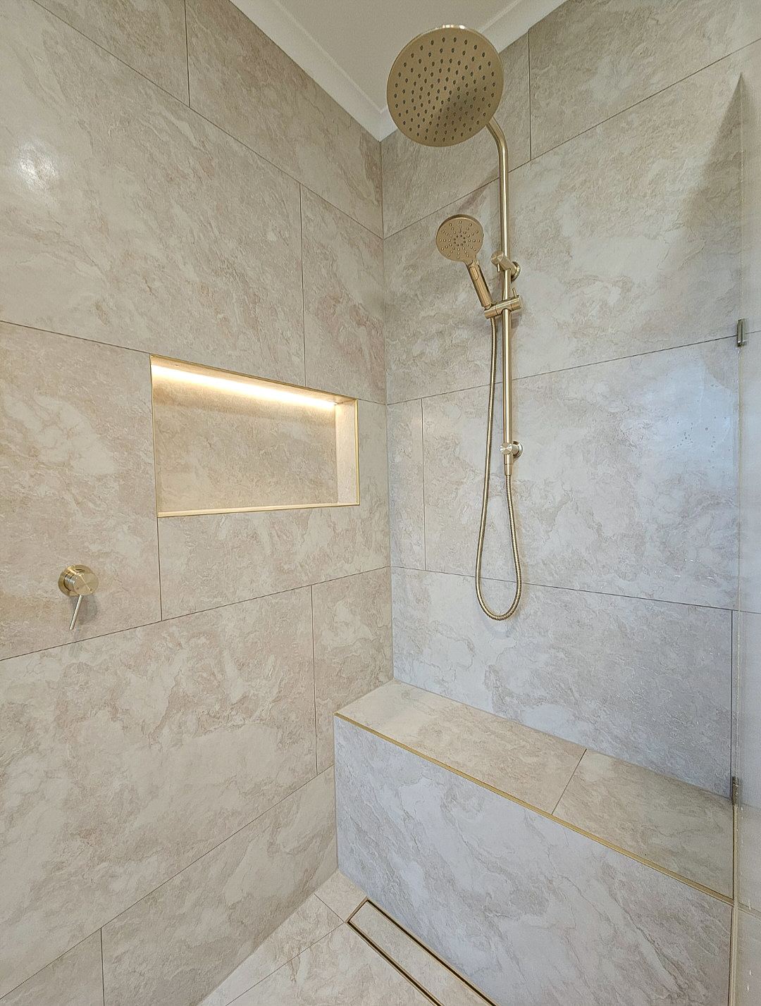 Luxury bathroom renovation in Melbourne with brushed gold fittings, marble-look tiling and a backlit niche